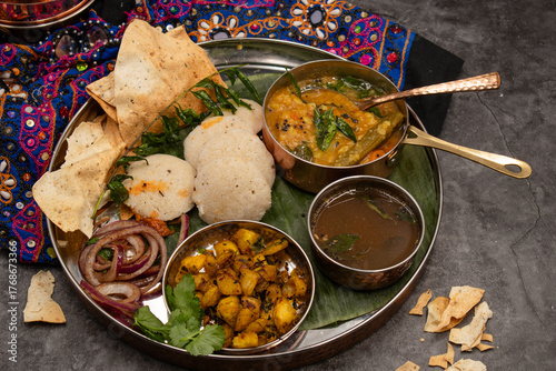 Festive plant based South Indian thali consisting of moringa sambar, ginger rasam, fermented idli- rice cakes, potato curry and side pickles