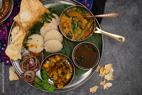 Festive plant based South Indian thali consisting of moringa sambar, ginger rasam, fermented idli- rice cakes, potato curry and side pickles
