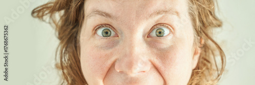 Caucasian female adult with wide green eyes and curly hair expressing surprise close-up.