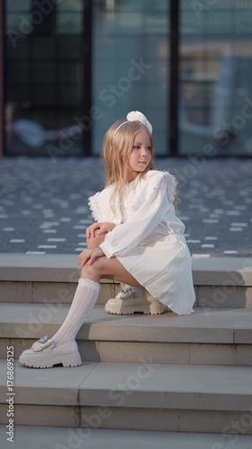 Little girl in a white dress sitting on the stairs. Cute child concept.