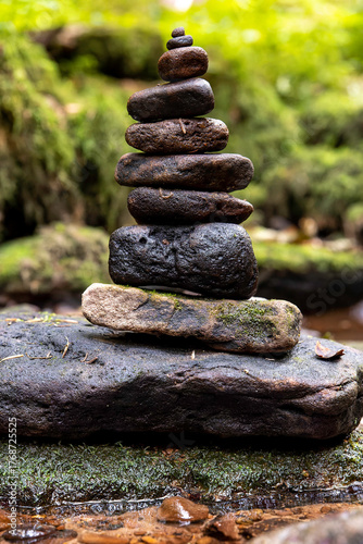 Balanced stones stacked carefully beside a serene stream in a lush green forest setting