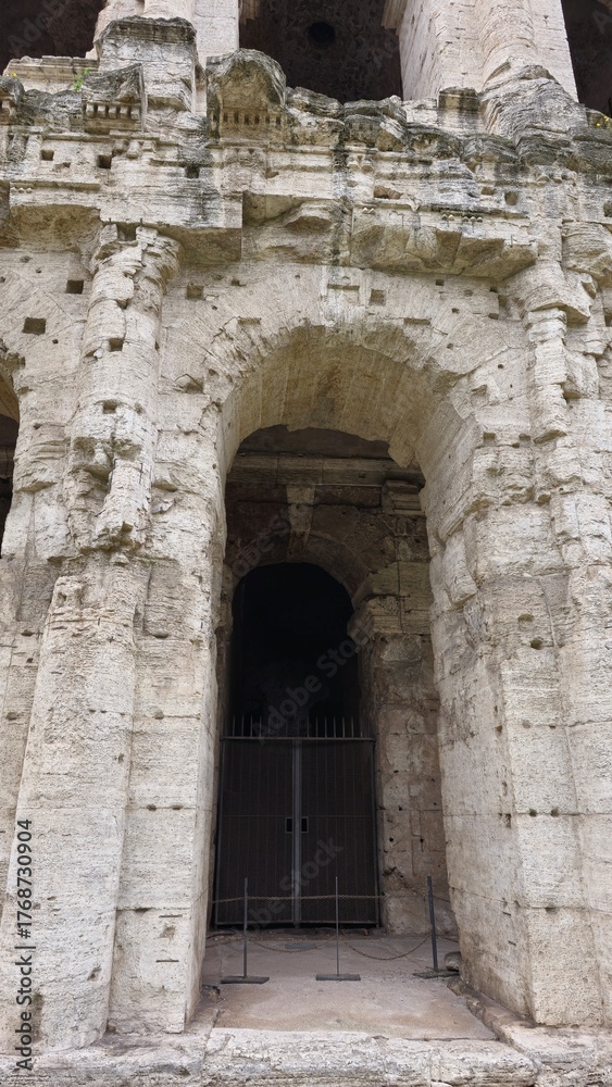 Fototapeta premium Rome, Italy - 11 January 2025. This close-up shows a gated archway at the base of the Theatre of Marcellus, surrounded by weathered limestone and architectural details above.