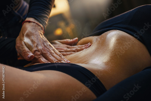 A professional therapist performing a wood therapy (maderotherapy) massage using a wooden roller on a woman's legs, belly and glutes