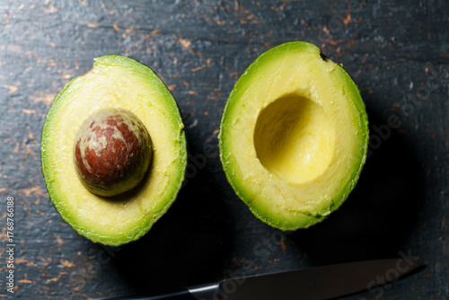 ripe avocado cut in half on a dark stone textured surface.