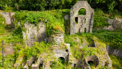 Crumbling stone walls and arches of the historic Clydach Ironworks covered in dense green foliage