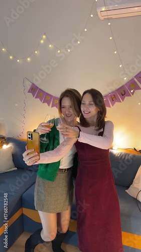 Friends making photo and checking messages during birthday celebration in decorated living room, cheerful moment with cozy lighting
