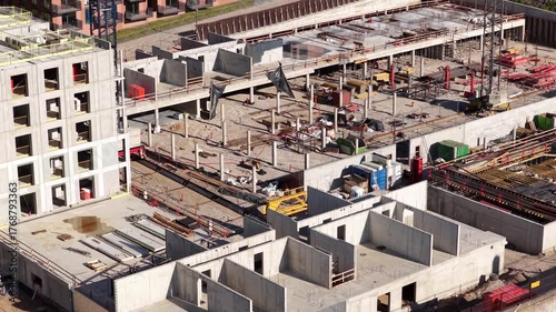High-angle view of a large urban construction site featuring reinforced concrete structures, support columns, cranes, scaffolding, and materials during mid-phase development.