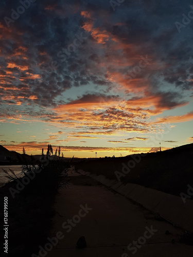 A golden sunset stretches over a long valley crossed by a pass: the sun kisses patterned clouds, bathing them in gold while foreground shadows add depth.