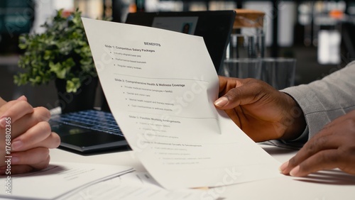 Close up of black man reads monthly perks and salary options, meeting with a recruiter to discuss the benefits package for health insurance and wellness programs within contract deal.