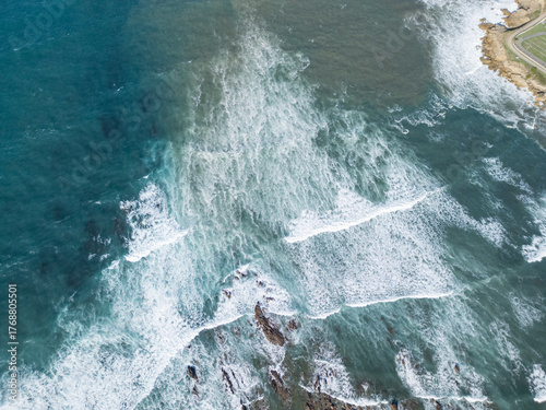Top down aerial view of turquoise ocean waves and sea foam on rocks. Abstract natural water texture background.