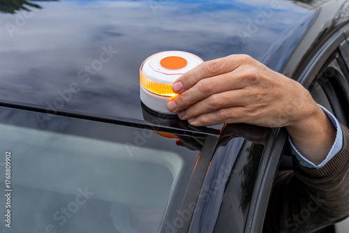 Driver hand placing connected V16 emergency warning beacon on car roof in Spain.
