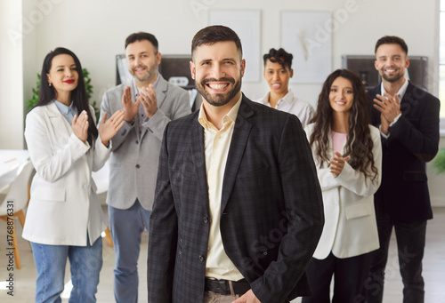Photos Confident young man standing in front of diverse team members applauding, clap hands, congratulating male colleague with professional success, career growth and promotion