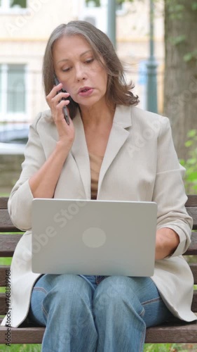 Old Senior Woman Talking on phone and Using Laptop in Park