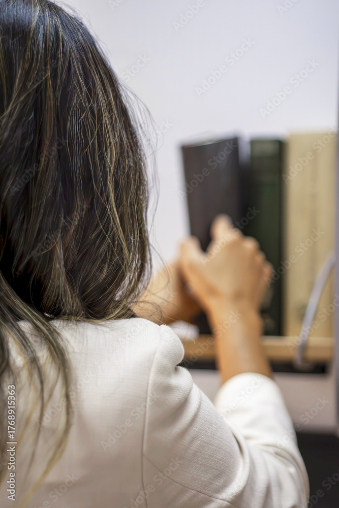 Fototapeta premium Woman selecting book from library bookshelf for reading