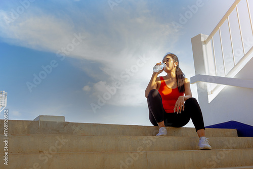 Tired runner woman with a bottle of electrolyte drink freshness after training outdoor workout at the stadium stairway.