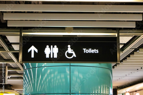 Black signs with white letters symbol icon for modern public toilet or bathroom hanging under ceiling at subway station in Hong Kong. Icon man, woman, people disabilities with person icon.