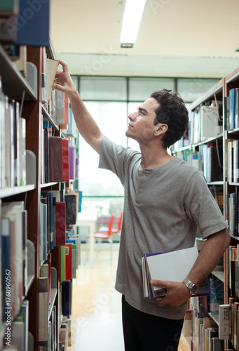 A young man stands between the shelves of a library