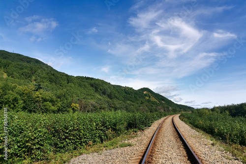 Railway track curves through dense green forested hills. A single railway track curves into the distance, surrounded by lush green hills and shrubs