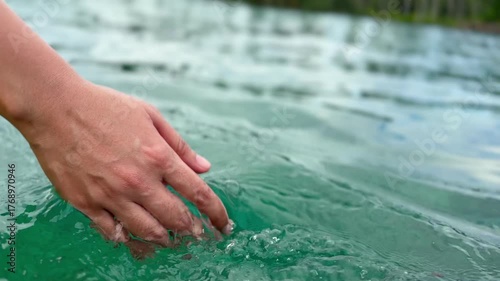 Hand of woman gently touches the surface of the clear blue-green water, creating gentle ripples. This concept conveys a sense of connection with nature, tranquility, and coolness.