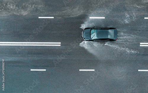 car is driving fast with spray on a flooded road after a downpour. aerial top view from flying drone.