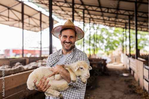 Male farmer holding smiling lamb in barn
