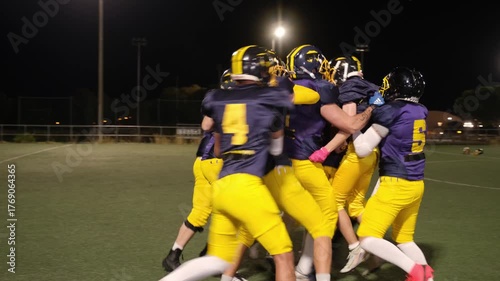Team of football players celebrating together after scoring a touchdown during a night game