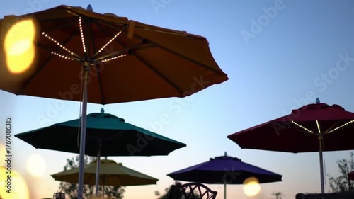 Colorful patio umbrellas glow with warm lights against a twilight sky, creating a festive outdoor ambiance.