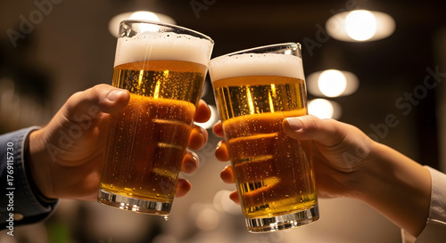Two people cheers with tall glass beers, light beer, frothy head, blurry background