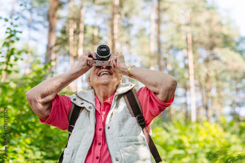 Elderly woman photographing nature during forest walk.