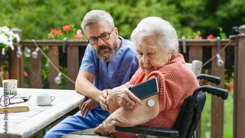 Photos Home nurse checking glucose level of senior lady with smartphone.
