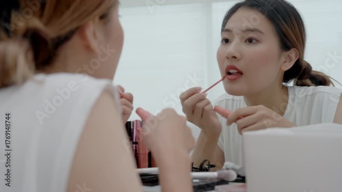 Beautiful Asian woman sit in front of a mirror and smile on makeup. face of a healthy woman applying makeup. Advertisement, lifestyle , cosmetics, makeup accessories, beauty activity, beautician