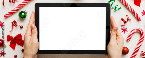 Christmas online shopping from home, female hands holding tablet pc with blank white display top view. woman hand holding tablet with blank screen, Christmas tree and gifts on background