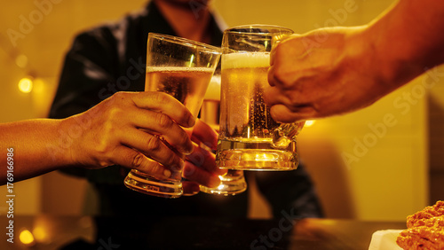 Close up friends hands clinking beer glasses in warm golden light, celebrating friendship teamwork. A joyful moment filled with laughter, unity, positive energy during relaxing evening gathering.