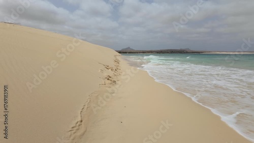 Waves breaking against sand dunes as they meet the sea on the shoreline of the Cape Verde island of Boa Vista.