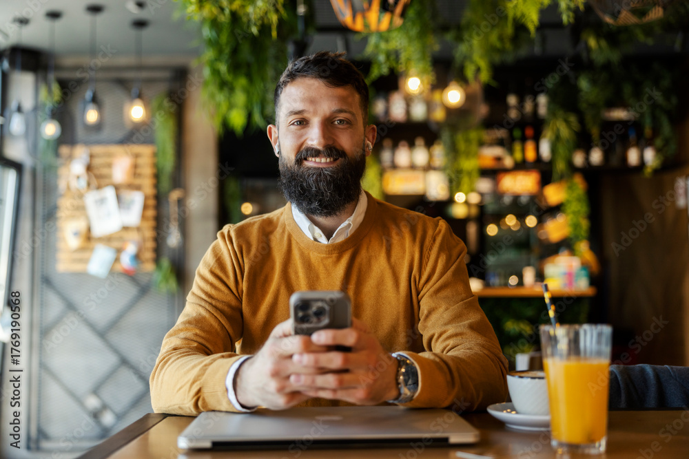 © Dusan Petkovic - Portrait of smiling business casual man sitting in cafeteria with cellphone in hands and looking at the camera.