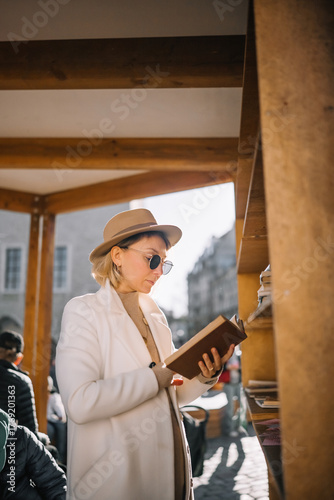 Woman browsing books at a cozy outdoor market in a sunlit historic area