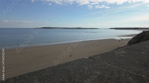 Tenby south beach at low tide with Caldey Island in the distance on a bright sunny day.