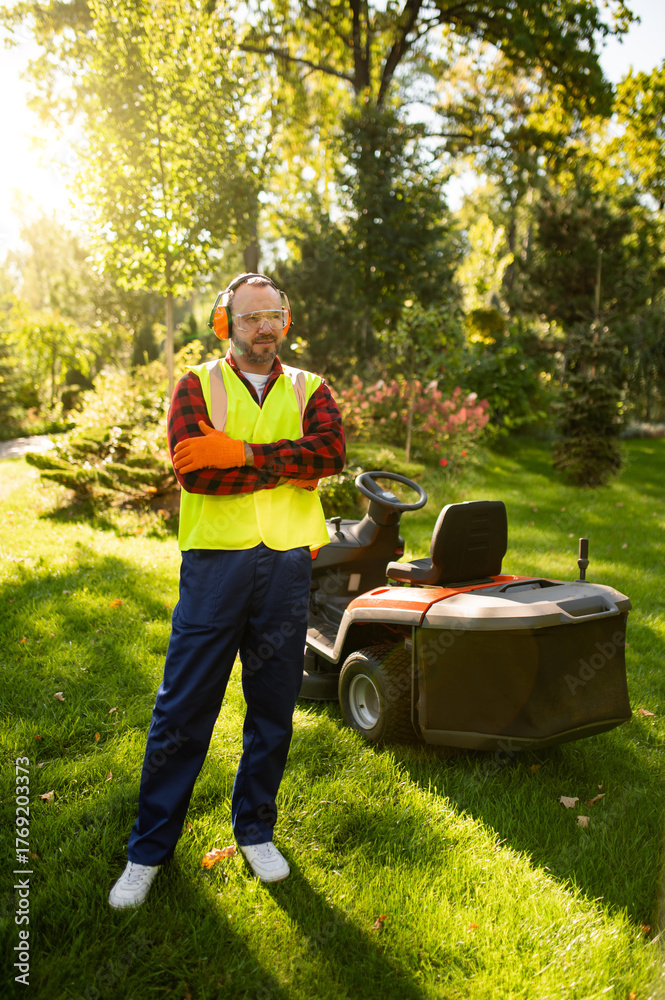 Fototapeta premium Confident man gardener posing with grass mower