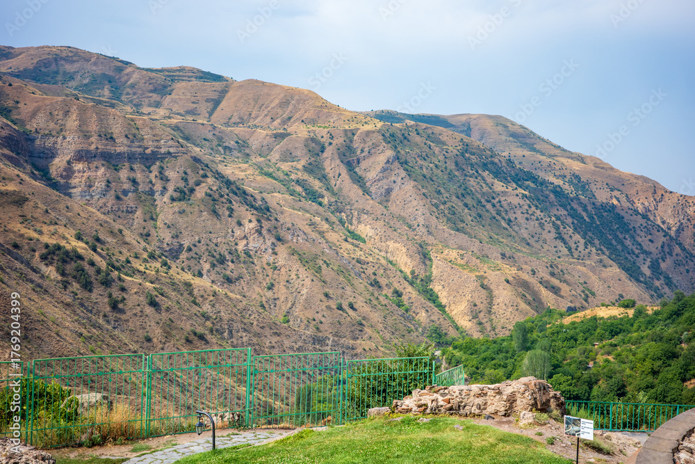 Fototapeta premium Panoramic view of the rugged Garni Gorge mountains in Armenia, showcasing the dry golden slopes and sparse green vegetation under a bright summer sky