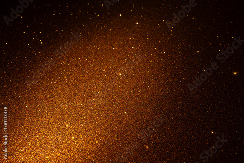 Shimmering golden glitter texture glowing diagonally, sparkling particles shine vividly and dissolve into dark edges forming luxurious abstract backdrop