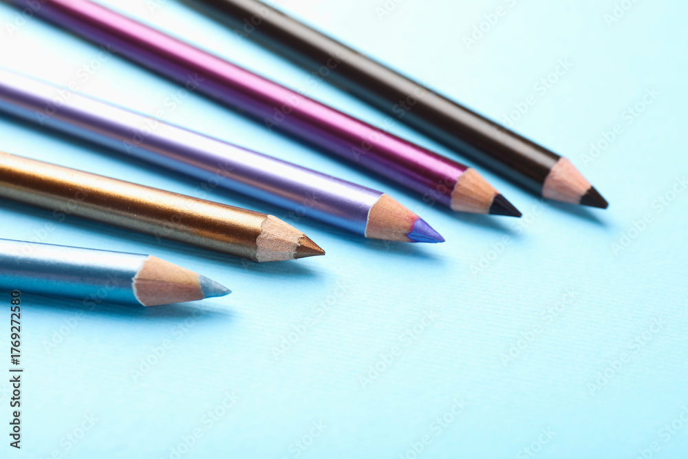 Fototapeta premium Eye pencils on light blue background, closeup