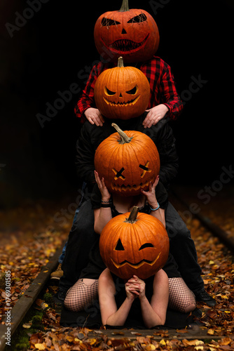 Four friends celebrate Halloween with stacked pumpkins on a railway surrounded by autumn leaves at dusk