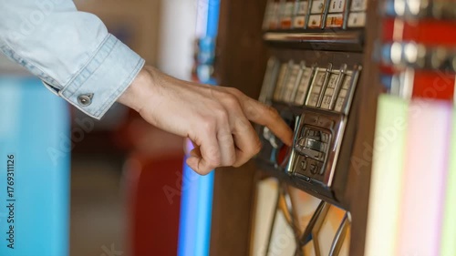 Close-up of a man's hand choosing a song by pressing a button on a retro jukebox in a diner.