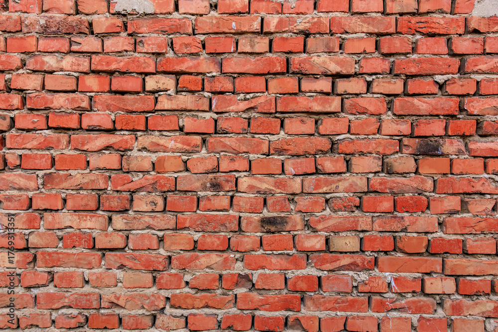 Obraz premium Red brick wall with weathered surface in urban setting