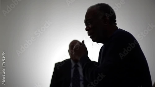 Two silhouetted figures in dark conversation against bright backdrop