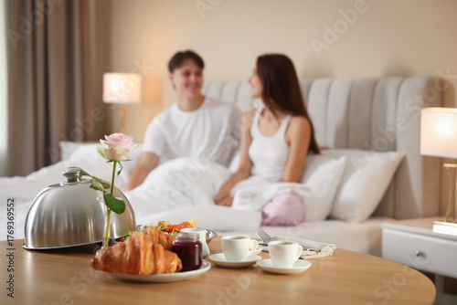 Fotografi Delicious breakfast served on wooden table and couple staying in bed at hotel ro
