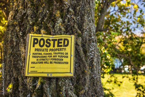 Yellow posted private property sign nailed to a tree trunk, warning against trespassing, hunting, and fishing on private land