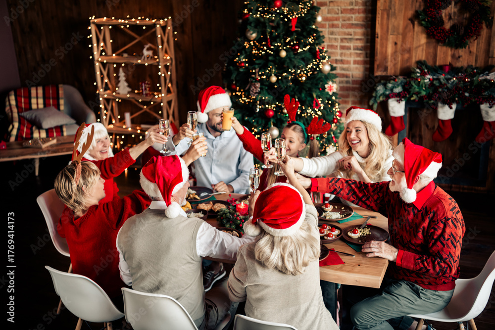 © deagreez - Christmas family dinner around a festively set table toasting with friends and relatives near a Christmas tree by a cozy fireplace