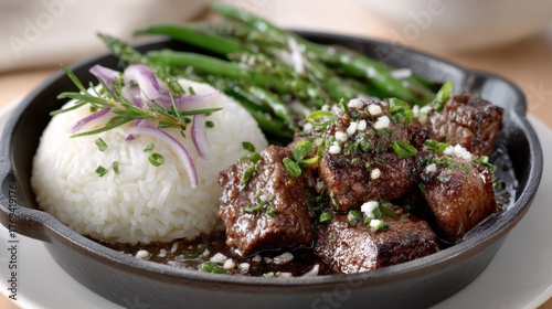 Delicious beef tips with rice and green beans garnished with fresh rosemary and onions in a skillet