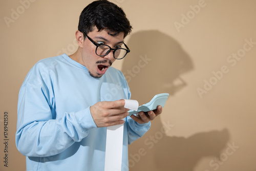 Photos Man with glasses holding a bill and a blue calculator, looking surprised with hi